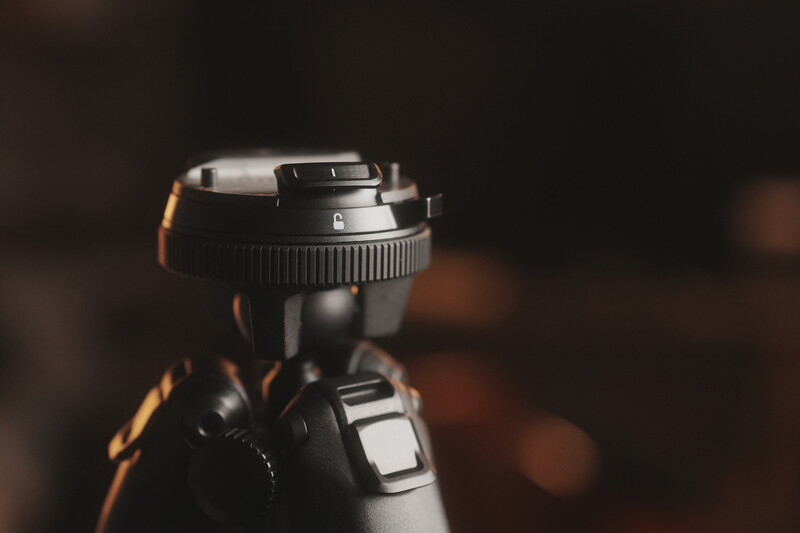 Close-up of a camera lens and flash unit with warm, directional lighting against a blurred background.