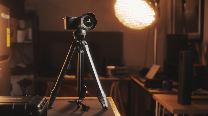 Professional camera on tripod in a studio setup with warm lighting and studio equipment visible in the background.