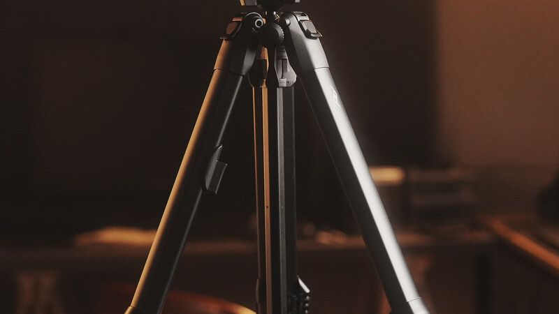 Professional tripod legs extended against a warm, blurred background with studio lighting.