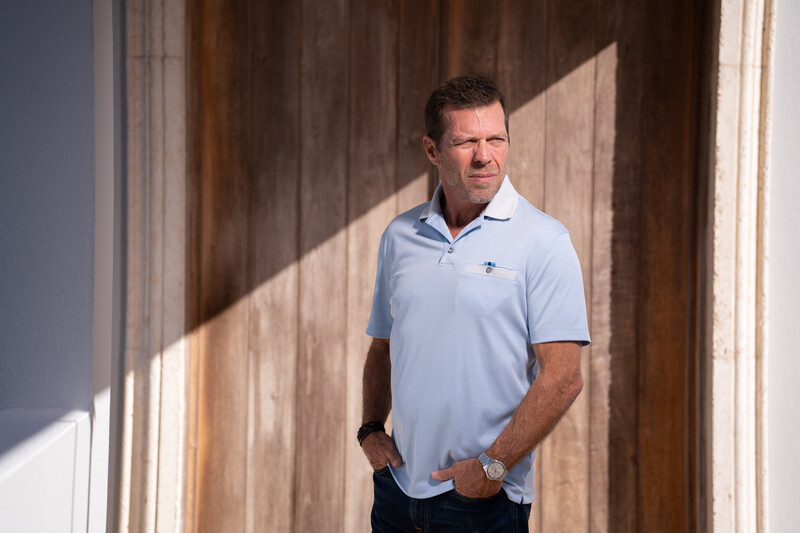 Man in light blue polo shirt standing in hallway with dramatic window light and shadow.