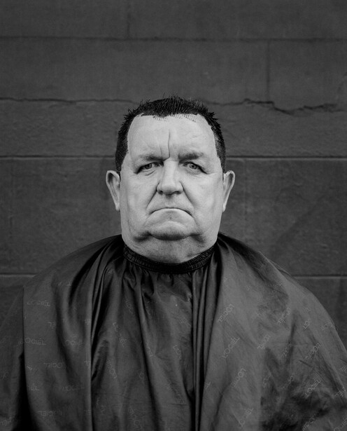 Black and white portrait of a man with a stern expression against a textured wall background.