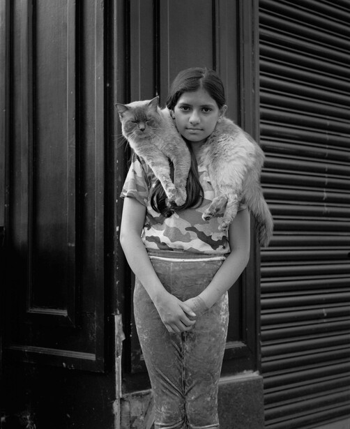 Woman holding a large cat while standing against a corrugated metal backdrop in black and white.