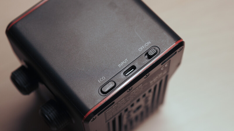 Close-up of a compact black device with red accents showing control buttons labeled Eco, Input, and Off on its top surface.