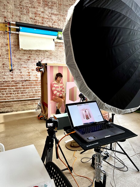 Portrait photography setup with large softbox, studio lights, tripod, and laptop showing live preview on brick wall backdrop.