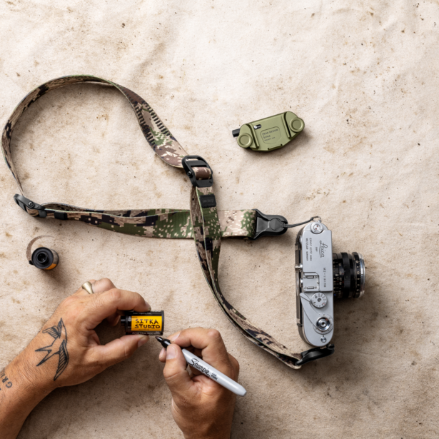 Hands holding a light meter next to a vintage rangefinder camera and accessories on concrete.