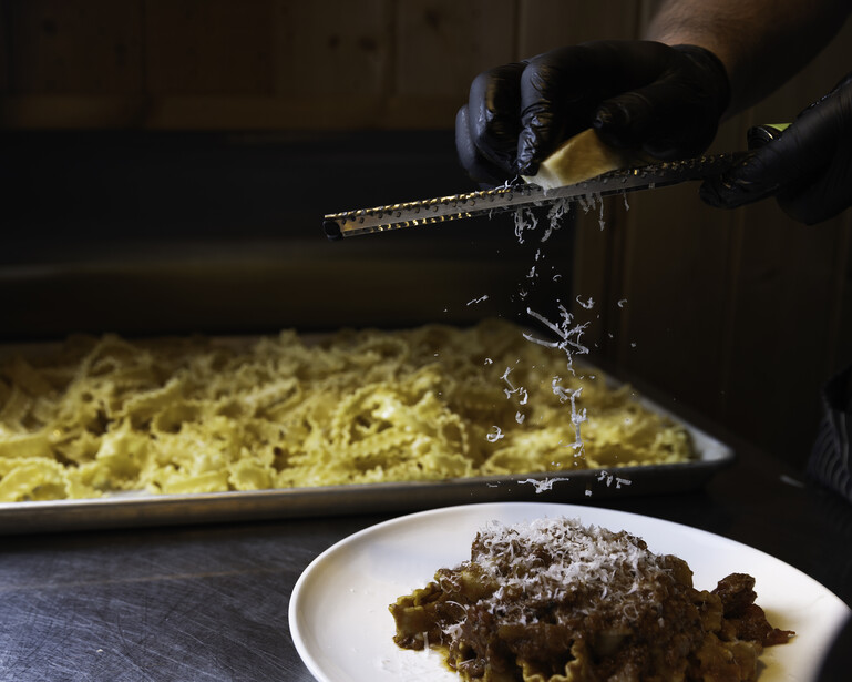 Chef grating cheese over a plated dish with pasta in background.