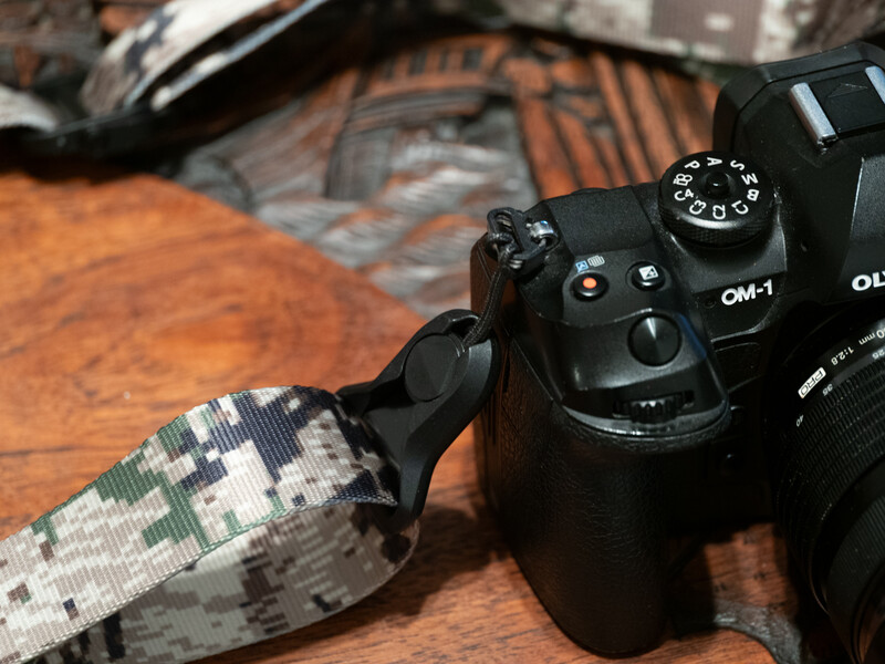 Olympus OM-1 camera with vintage patterned strap on wooden surface.