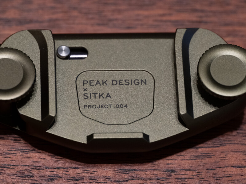 Peak Design Sitka Project .004 camera strap connector displayed on wooden surface.