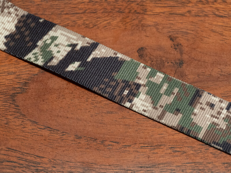 Camouflage-patterned ribbon with white, black, and olive green colors on wooden surface.
