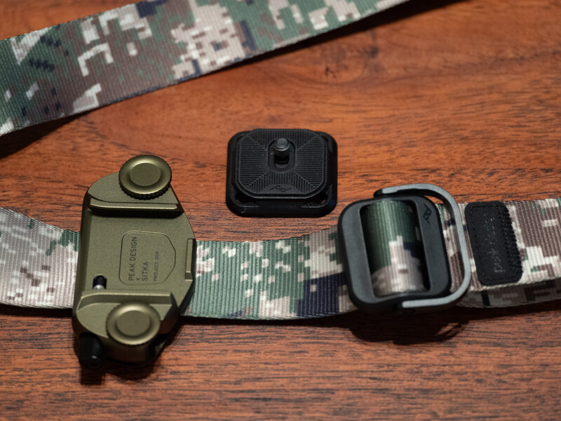 Three camera flash triggers and sync cables arranged on a wooden surface with digital camouflage webbing.