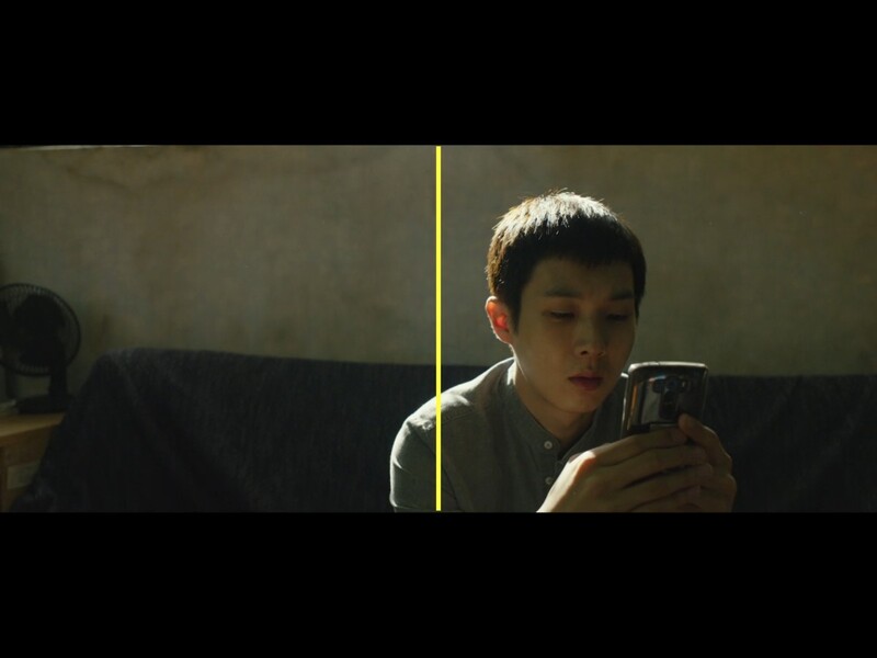 Young man in brown shirt holding smartphone, lit by warm directional light against dark background.