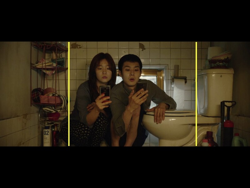 Two people in a bathroom mirror reflection, both with surprised expressions and hands raised to their chests.