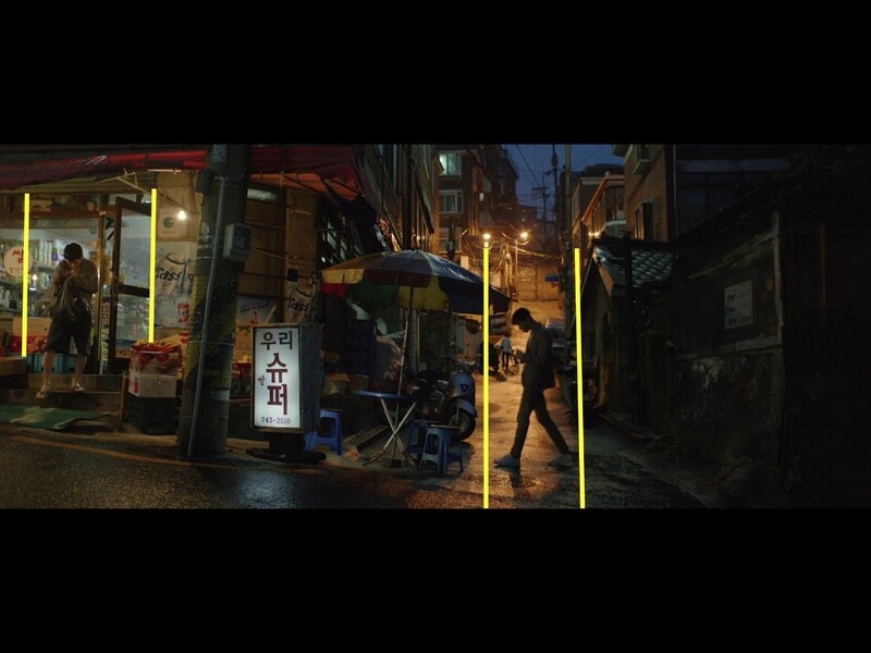 Nighttime street scene with illuminated storefronts and pedestrians walking through a narrow urban alley.