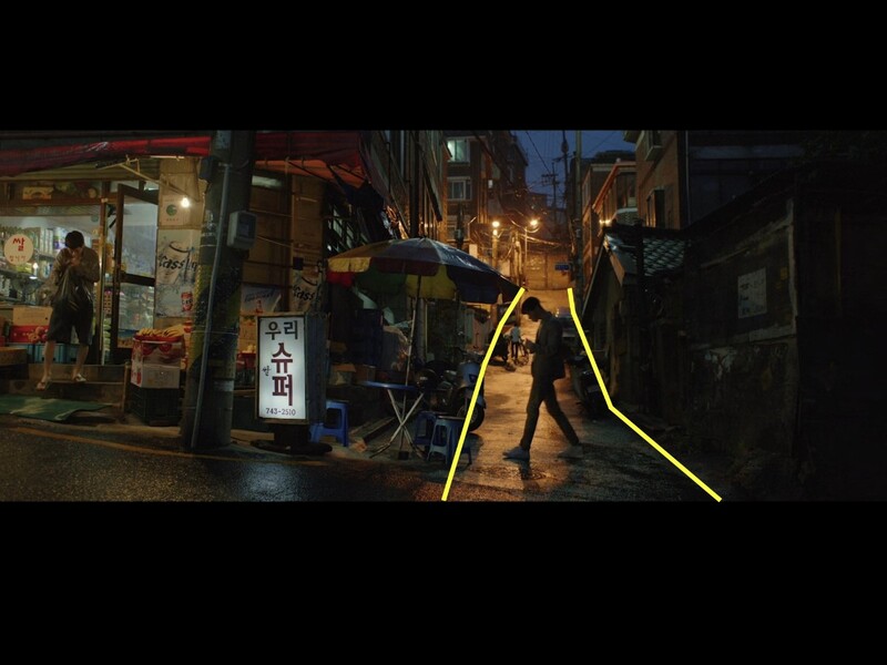 Nighttime street scene in an Asian alleyway with neon yellow light trails and pedestrians among storefronts.