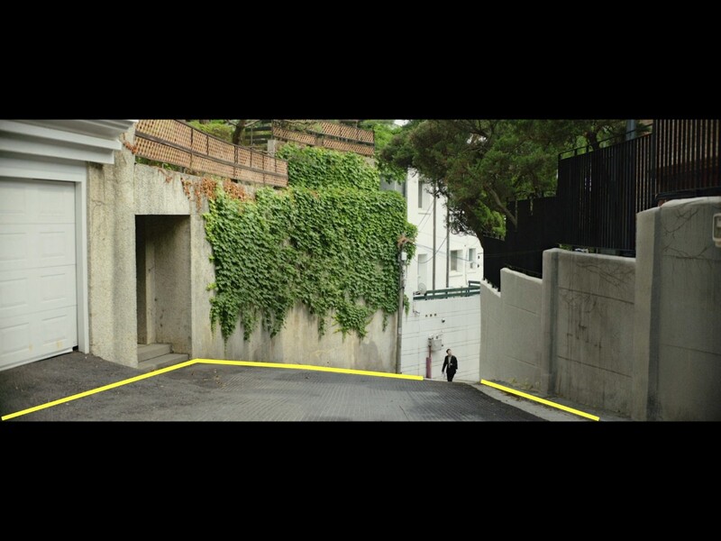Urban alleyway with yellow guide lines overlaid on pavement, ivy-covered brick wall, and concrete structures.