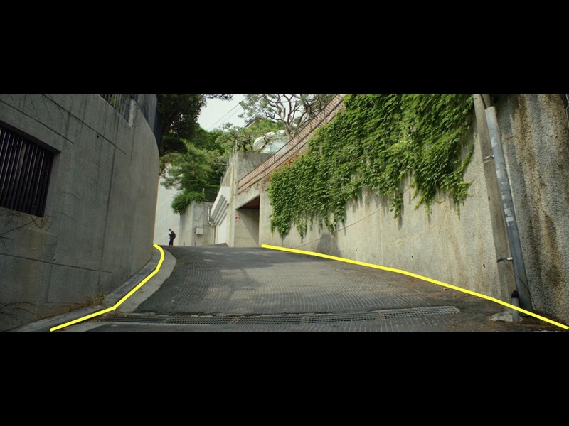 Narrow urban alley with yellow guide lines leading toward ivy-covered stone walls and buildings.