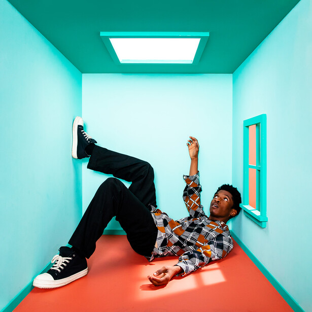 Two people in a bright turquoise corridor with an orange floor, one seated and one lying down with legs extended.