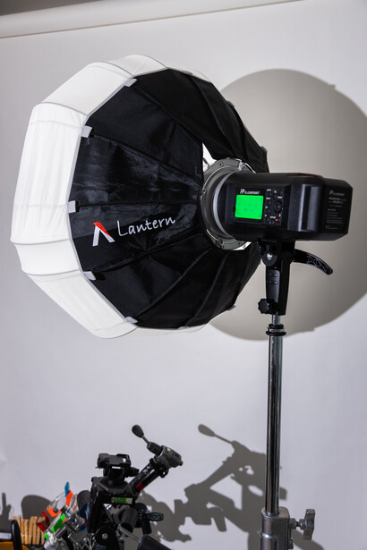 Studio lighting setup with a large parabolic softbox reflector and mounted flash unit on a stand.