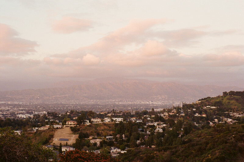 Hillside residential neighborhood overlooking a sprawling city covered in atmospheric haze.