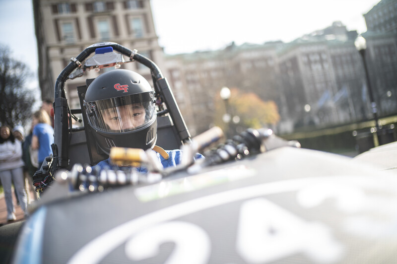 Dragster driver in full helmet and racing suit sits in cockpit of high-performance race car.