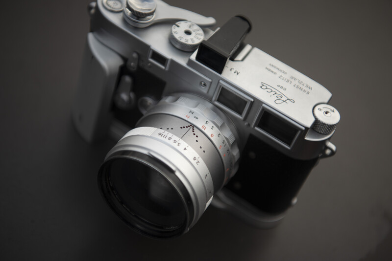 Vintage rangefinder camera with chrome body and attached lens, photographed from above against a neutral gray background.
