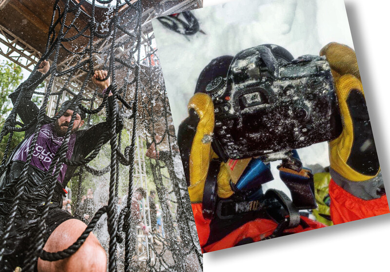 Underwater photographer in yellow and red wetsuit holding camera equipment near coral reef structure.
