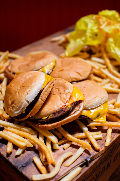 Burger with melted cheese and grilled onions served on french fries against a dark red background.