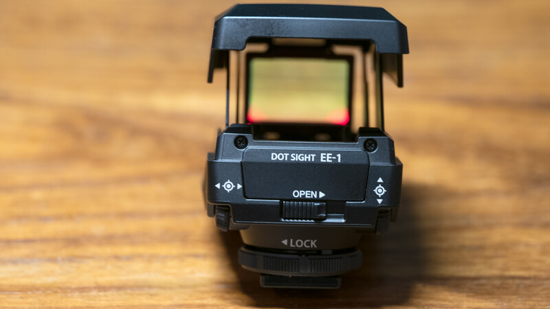 EOTech EE-1 holographic dot sight with amber reticle displayed on wooden surface.