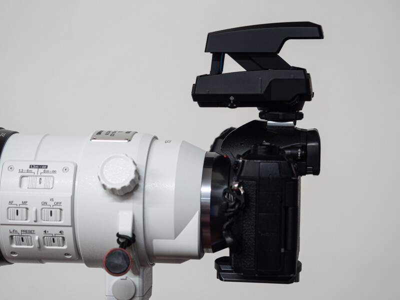 White telephoto lens mounted on black DSLR camera with flash attached on neutral background.