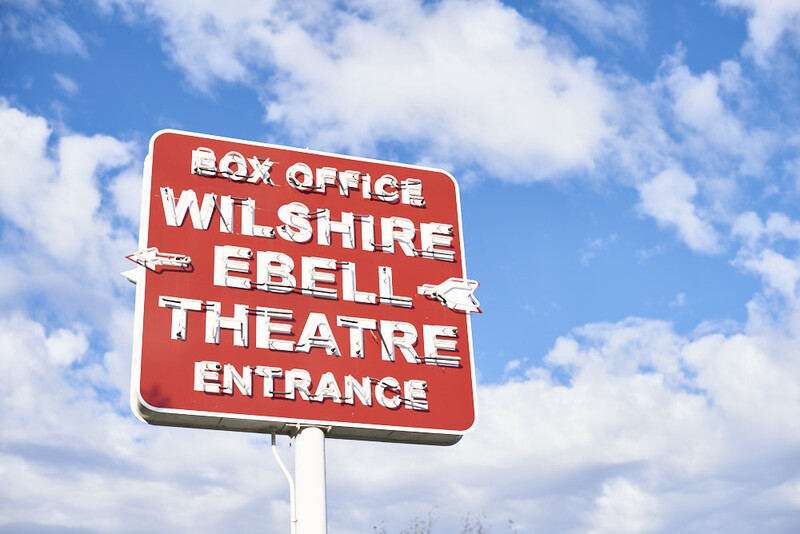 Red vintage sign with white text directing to Wilshire Ebell Theatre box office entrance.
