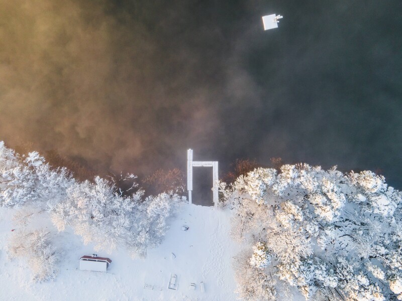 Aerial view of a snowy beach with a wooden structure and boats near the shoreline.