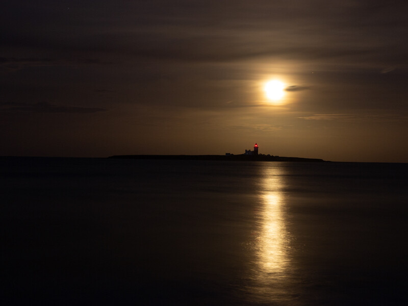 Full moon rising over a calm sea with a silhouetted island structure on the horizon.