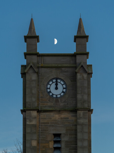Stone clock tower with two spires against blue sky and crescent moon.