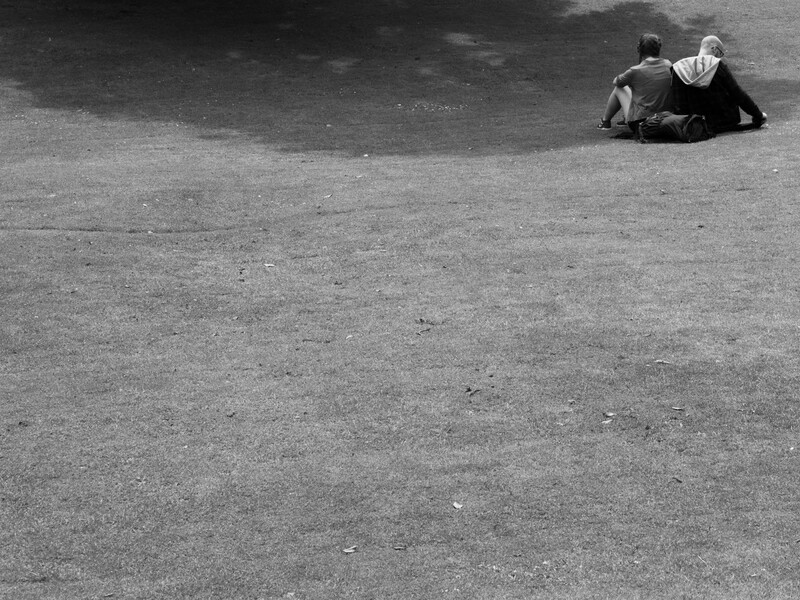 Person sitting alone on an empty asphalt surface in black and white.