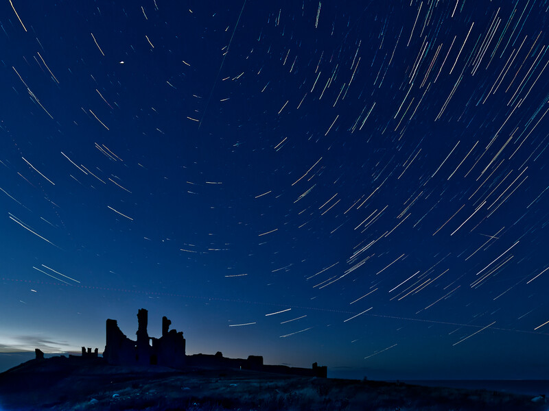 Silhouetted ruins against a night sky filled with concentric star trails from long exposure photography.