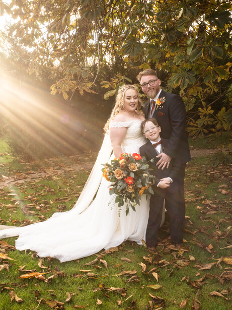 Bride and groom pose together outdoors in golden hour sunlight filtering through tree canopy.