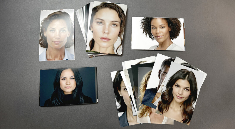 Printed headshot photographs and portrait proofs arranged on a gray surface.