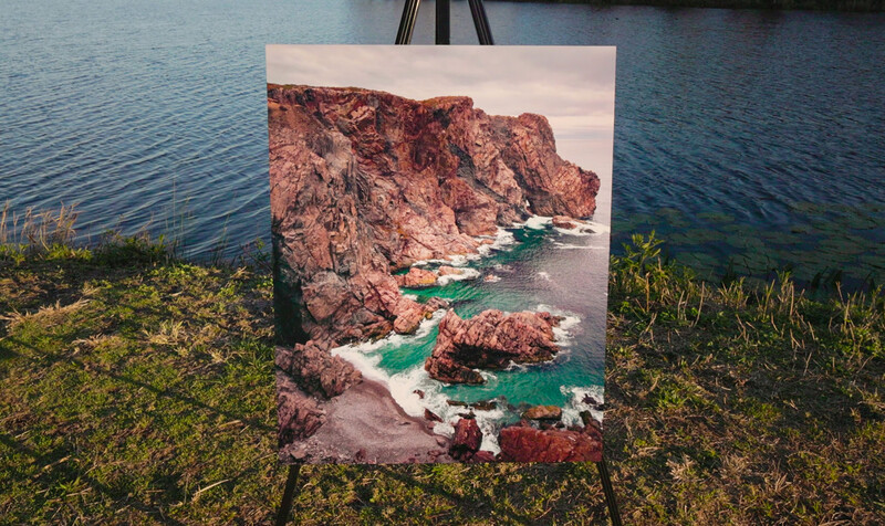 Printed photograph of rocky coastal cliffs and turquoise water displayed outdoors on an easel.