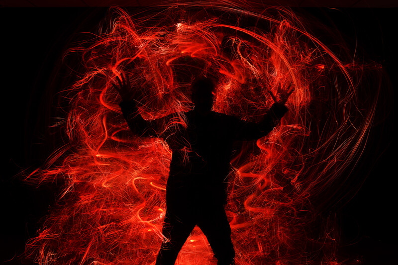 Silhouetted figure standing against dramatic red and orange light trails creating an explosive, energetic background.