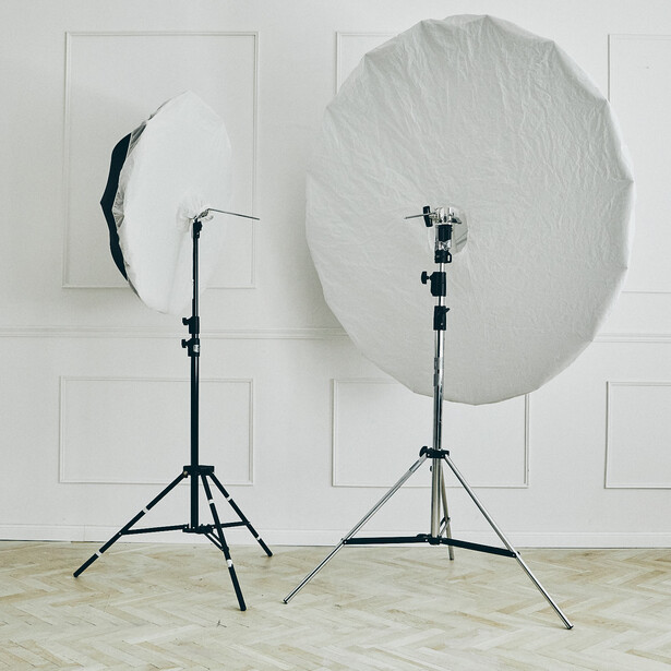 Two studio lighting setups with tripod stands and diffusion modifiers against a white wall.