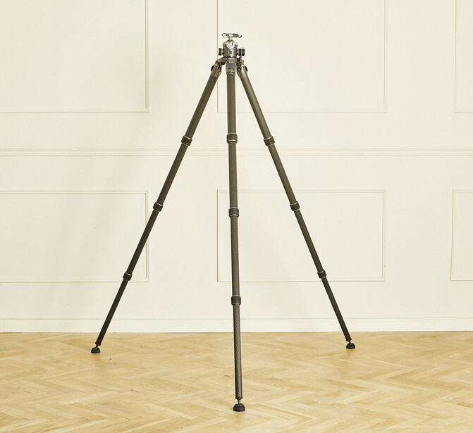 Sturdy tripod with dark metal legs and center column against neutral studio backdrop.