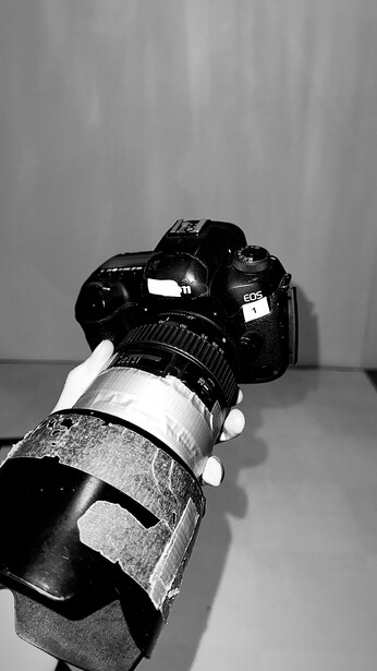 DSLR camera with attached telephoto lens and lens hood positioned on gray surface against neutral background.