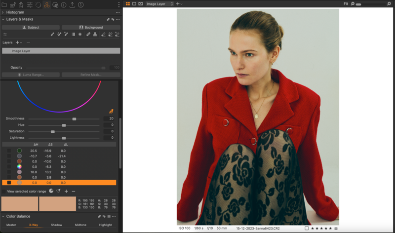 Woman wearing red blazer and patterned teal dress in studio portrait setup.
