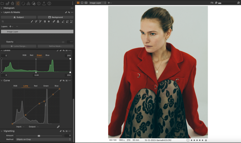 Woman wearing red blazer and patterned blue dress photographed against neutral background.