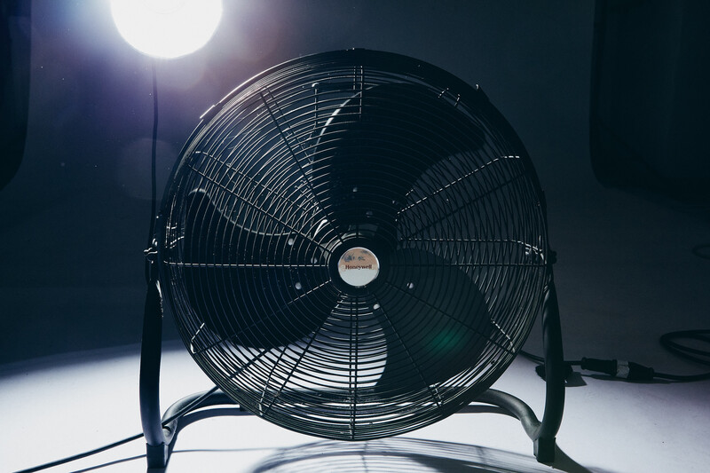 Industrial floor fan photographed against bright backlight with dramatic side lighting and dark background.