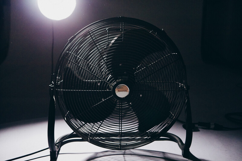 Black industrial fan photographed against bright backlit lighting in a dark studio setting.