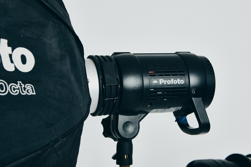 Profoto studio flash mounted on a light stand next to a dark blue equipment bag.