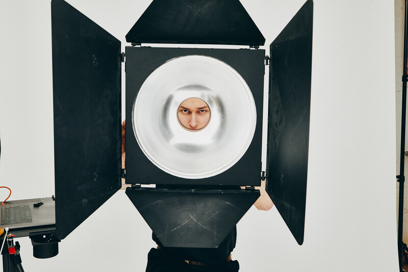 Man's face framed by white circular reflector inside open black studio light with barn doors.