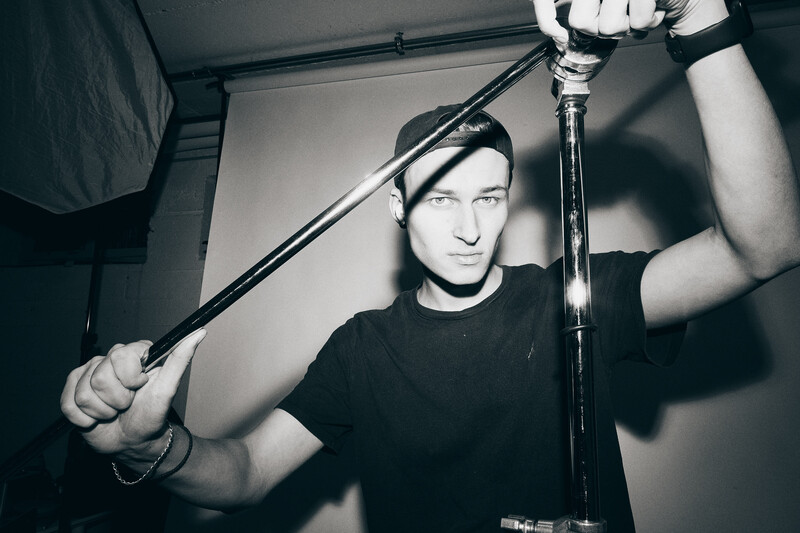 Man holding microphone boom in recording studio with overhead lighting setup.