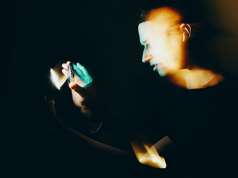 Two illuminated faces against a dark background, one holding a glowing device.